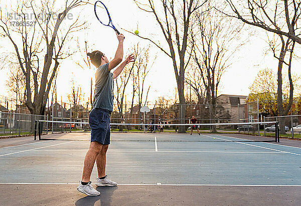 Teenager spielt im Frühling Tennis auf einem Hartplatz im Freien.