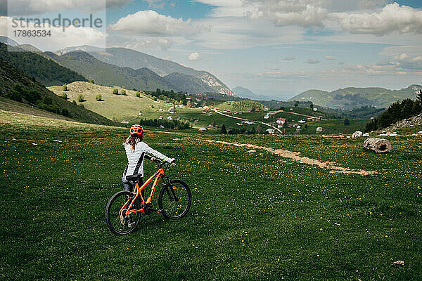 Radfahrerin mit Helm hält ihr Fahrrad und blickt ins Tal