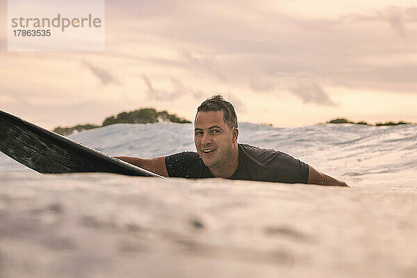 Porträt eines glücklichen Mannes  der auf einem Surfbrett am Meer liegt