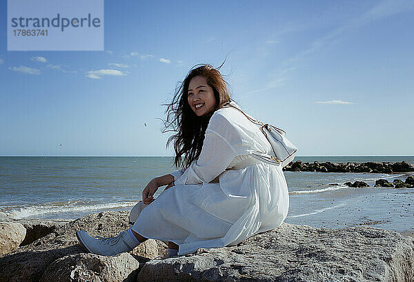 Schöne asiatische Frau saß im Sommer auf einigen Felsen am Strand