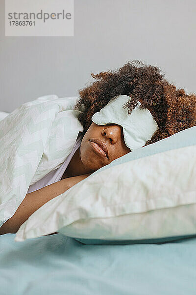 Lockige Afrikanerin schläft in Wohnung mit Schlafmaske im Gesicht.