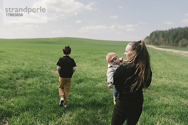 Eine Frau geht mit ihren Kindern auf einer grünen Wiese spazieren