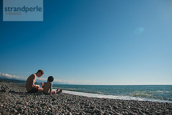 Ein kleiner Junge und sein Vater sitzen am Meer und reden.