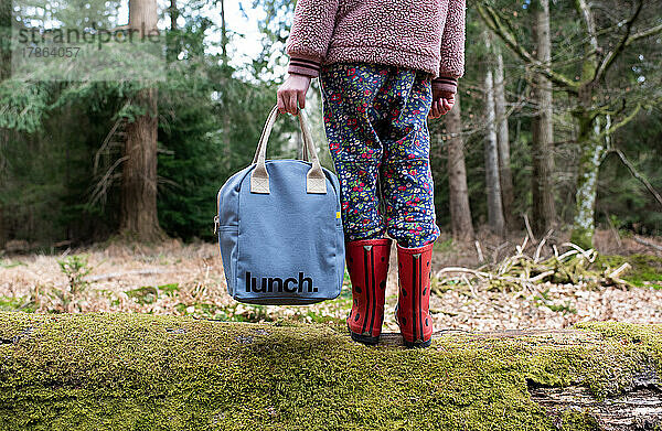 Kind hält sich beim Spaziergang im Wald an einer Picknicktasche fest