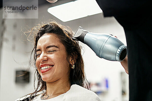 Friseur trocknet Haare eines fröhlichen Kunden