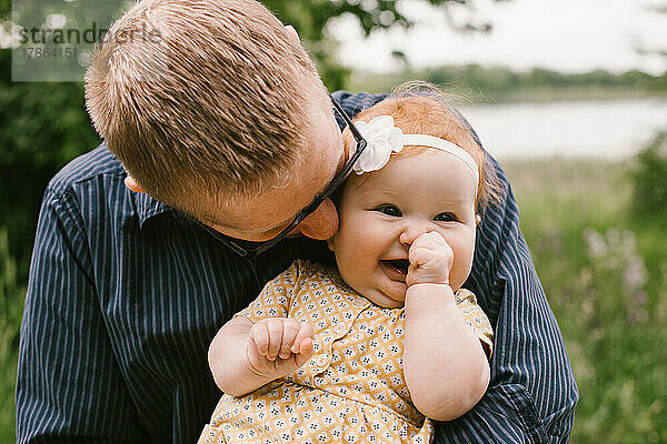 Die kleine Tochter lächelt und lacht  während der Vater sie hält und umarmt
