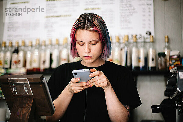 Weibliche Barista benutzt Smartphone an der Kasse im Café