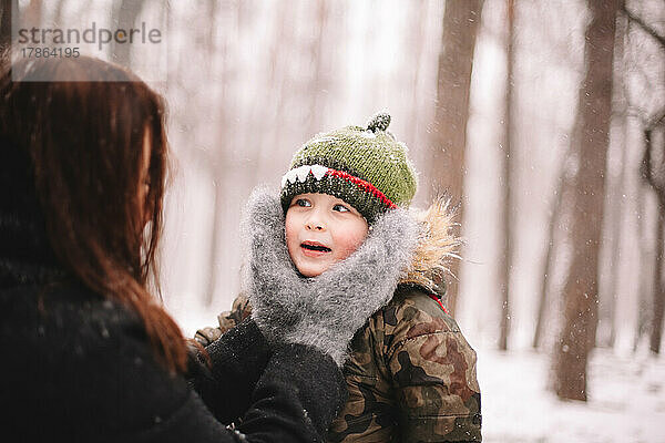 Baby Junge schaut Mutter an  während sie im Winter sein Gesicht hält