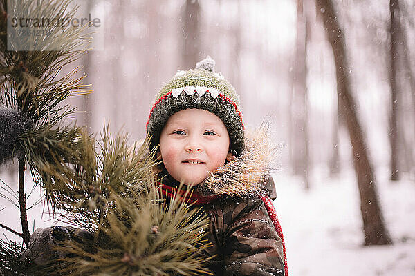 Niedlicher kleiner Junge  der im Winter draußen am Weihnachtsbaum steht