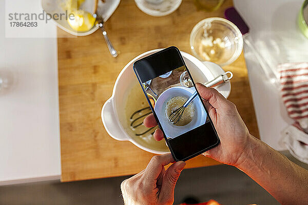 Frau fotografiert Essen mit Mobiltelefon in der Küche