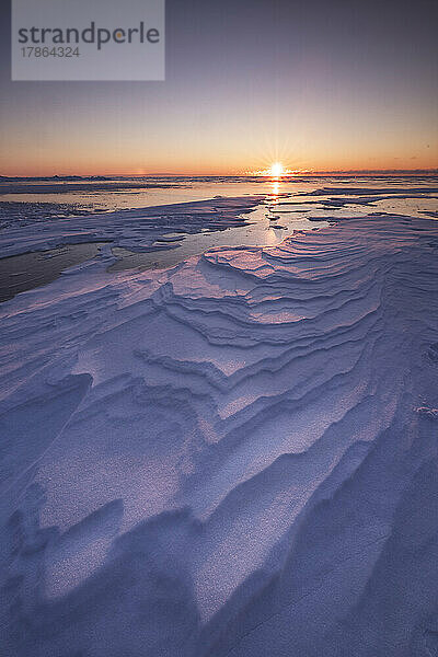 Risse im Schnee über dem zugefrorenen See bei Sonnenaufgang