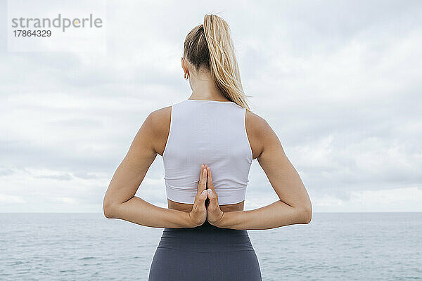 Rückansicht eines Mädchens am Strand  das Yoga macht.