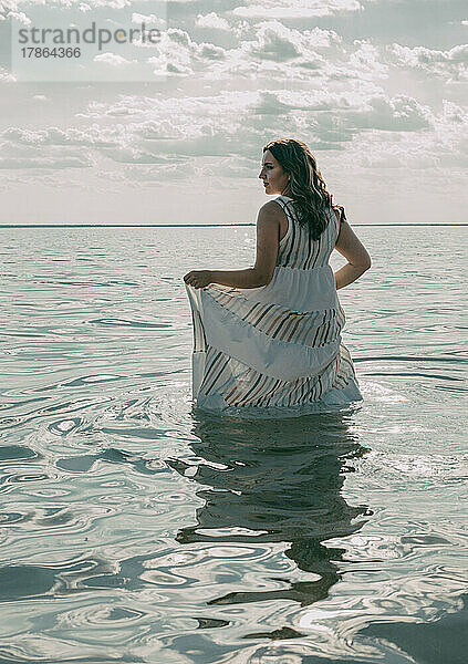 Elegante Frau stieg ins Wasser. Sonnenuntergang und Silhouette.