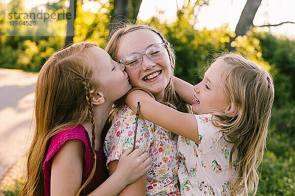 Junge Schwestern lachen  umarmen und küssen sich im goldenen Licht