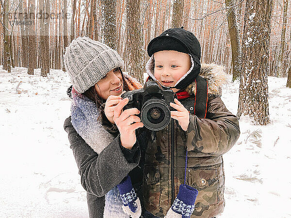 Glückliche Mutter und Sohn halten im Winter eine Digitalkamera im Park