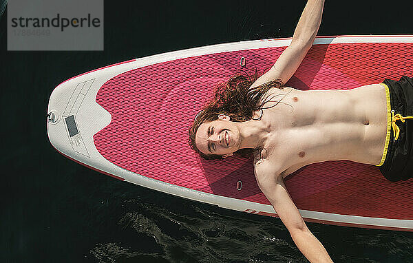 Draufsicht auf einen Mann mit langen Haaren  der auf einem Sup-Board im Meer liegt.