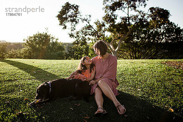 Mutter und Tochter posieren bei Sonnenuntergang im Park mit Hund in San Diego
