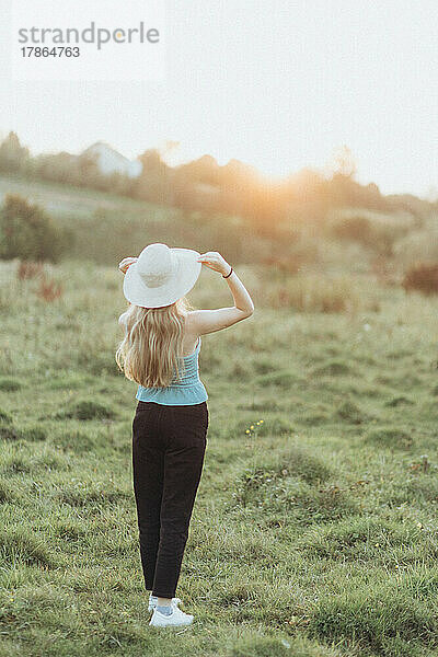 Frau in Jacke und Hut genießt allein den Sonnenuntergang