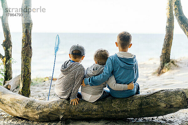 Drei Jungen sitzen auf einem Baumstamm und schauen auf das Meer
