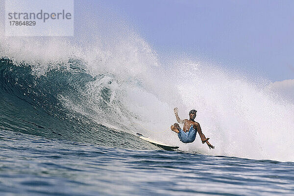 Asiatischer Surfer auf einer Welle an einem sonnigen Tag