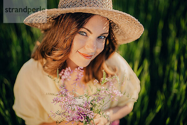Hübsche Landfrau mit Strohhut und Blumenstrauß auf dem Feld.
