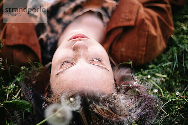 Nahaufnahme des Porträts eines friedlichen Teenager-Mädchens  das im Frühling auf Gras liegt