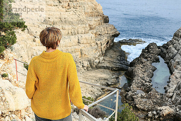 Ältere Touristenfrau beobachtet bei Sonnenuntergang Wellen auf Felsen