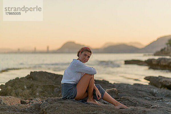 Junge Frau im Urlaub sitzt glücklich am Strand