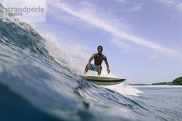 Asiatischer Surfer auf einer Welle an einem sonnigen Tag