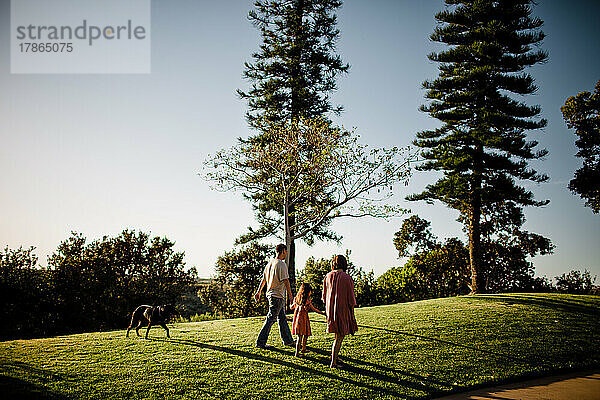 Dreiköpfige Familie spaziert mit Hund im Park bei Sonnenuntergang in San Diego