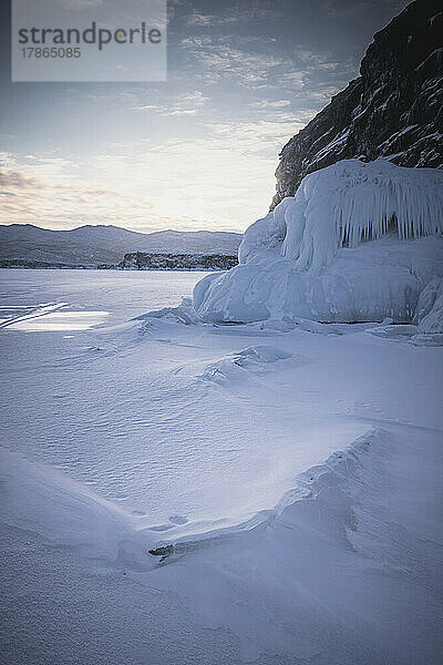 Eisiger und verschneiter Sonnenuntergang im zugefrorenen See