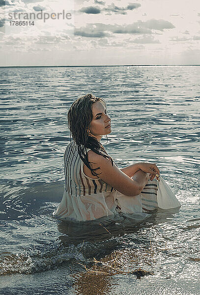 Elegante Frau sitzt im Wasser. Sonnenuntergang und Silhouette.