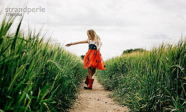 Junges Mädchen tanzt fröhlich in einem Käferkleid durch Maisfelder