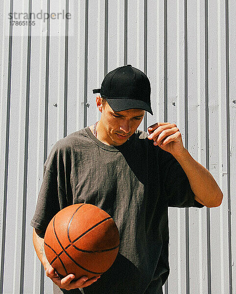 Stilvoller Typ in dunkler Kleidung und einer schwarzen Mütze mit einem Basketball