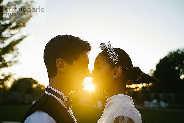 Multiracial couple touch noses in loving embrace with sunset