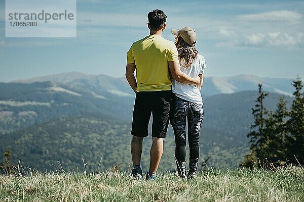 Rückansicht eines jungen sportlichen Paares  das sich umarmt und auf die Berge blickt