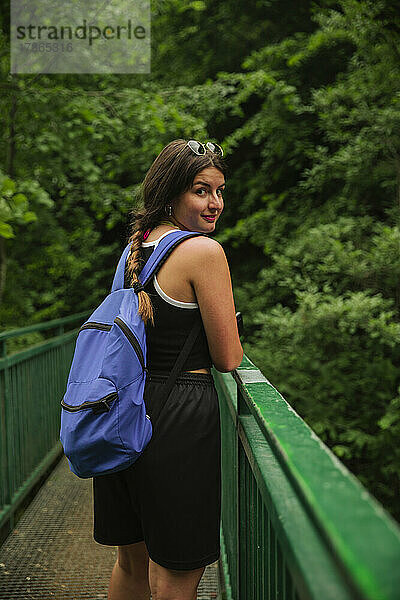 Wanderer schaut in die Kamera  während er eine Brücke in den Bergen überquert