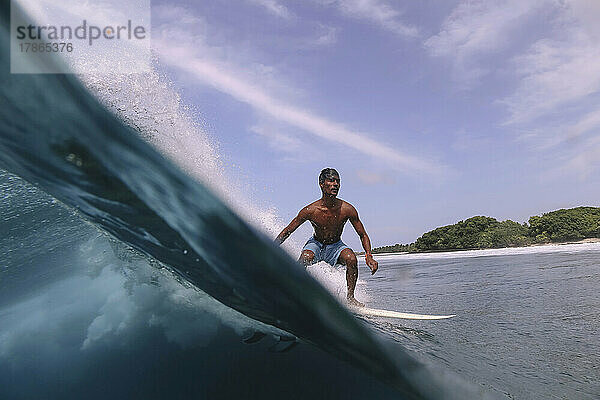 Asiatischer Surfer auf einer Welle an einem sonnigen Tag
