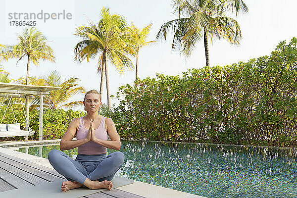 Eine Frau macht Yoga am Pool  sitzt im Lotussitz.