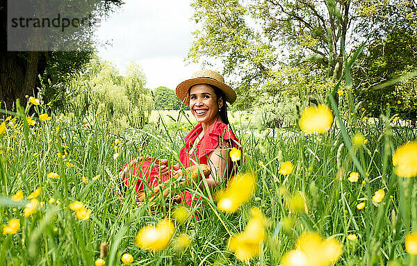 Schöne asiatische Frau sitzt glücklich auf einem Feld an einem sonnigen Tag
