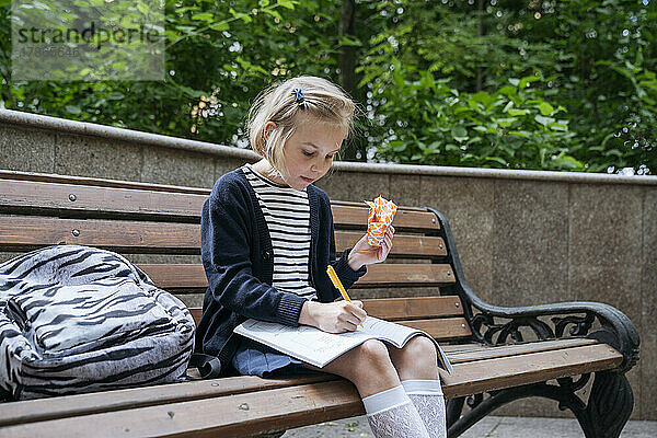 Das Mädchen macht ihre Hausaufgaben und isst ein Sandwich im Park.