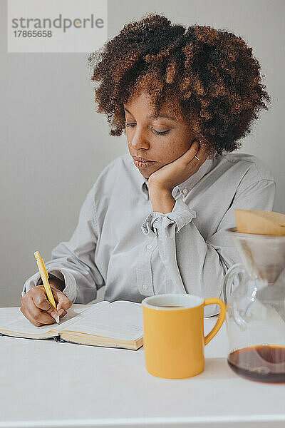 Eine lockige Afroamerikanerin macht sich beim Frühstück Notizen in ihrem Tagebuch.