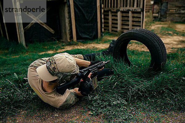 Soldat liegt im Gras und zielt in einem Airsoft-Match mit einer Waffe