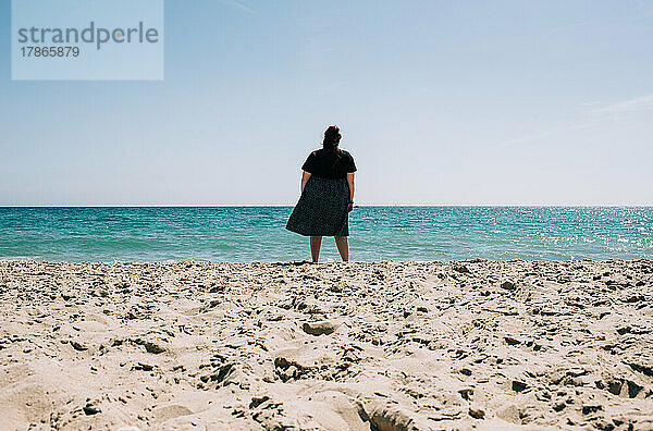 Eine Frau stand an einem sonnigen Tag allein im Sand und blickte auf das Meer