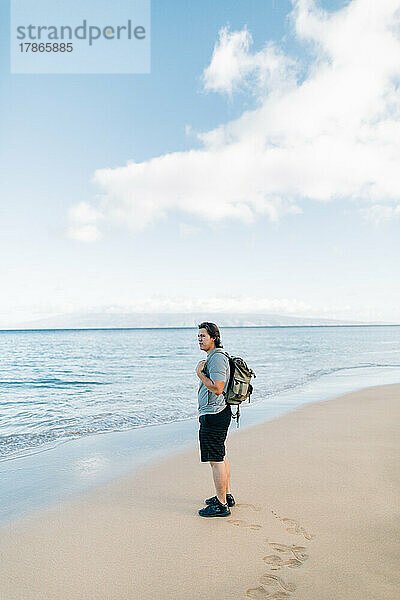 Indianischer Mann mit Rucksack steht am Strand in Maui H