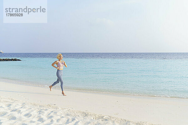 Athletische Frau joggt am Strand.