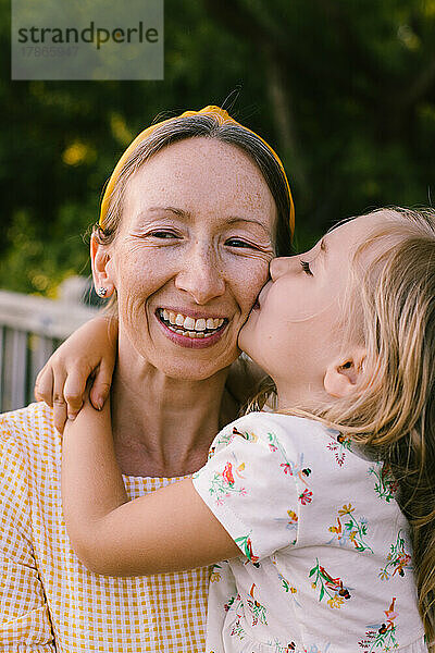 Junge Tochter gibt lächelnder  glücklicher Mutter einen Kuss auf die Wange