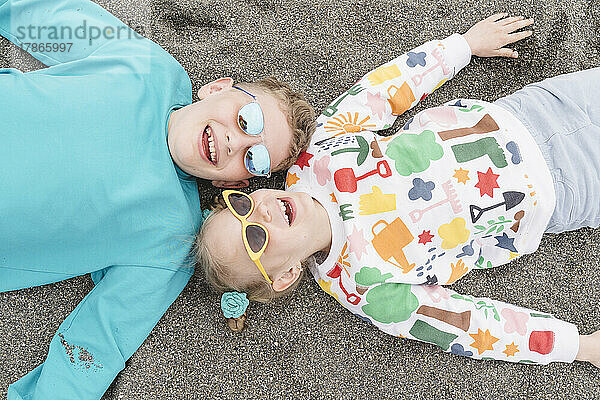 Bruder und Schwester liegen am Strand im Sand.