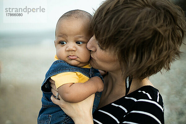 Newborn multiracial baby boy held and kissed by mother