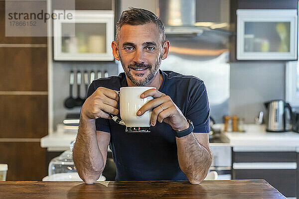 Ein gutaussehender Mann  der einen Kaffee trinkt und dabei in die Kamera blickt